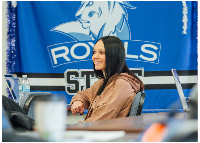 Student sitting in a classroom with a Lake Region State College Royals flag displayed on the wall behind her.