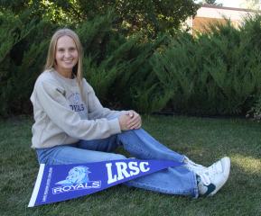 LRSC graduate Kassidy Hart poses on lawn with LRSC pennant