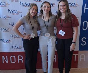 Sydney, Keira, and Sadie standing in front of HOSA screen