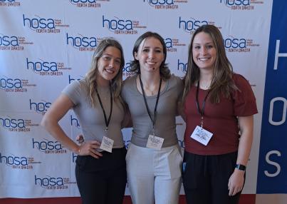 Sydney, Keira, and Sadie standing in front of HOSA screen